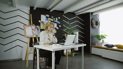 Young graphic drinking water and working on computer using tablet