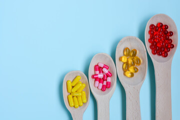 Four wooden spoons full of pills, vitamins, capsules, omega-3 fish oil,vitamin E, medicines and health supplements on a blue background.Copy space.