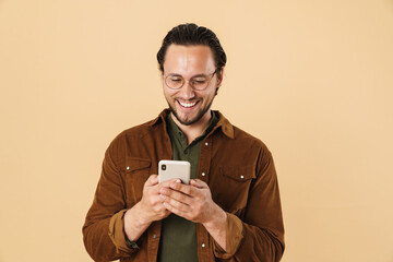 Image of excited bristle man in eyeglasses smiling and using cellphone