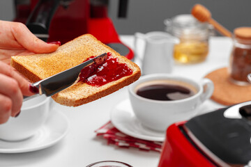 Female hand spresding strawberry jam on baked toast
