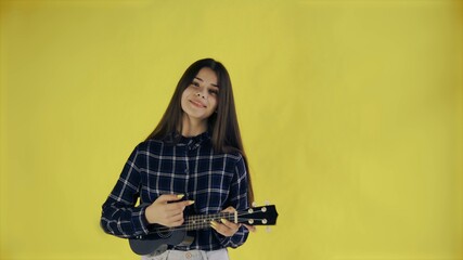 Young girl singing and playing ukulele on yellow Background in Studio
