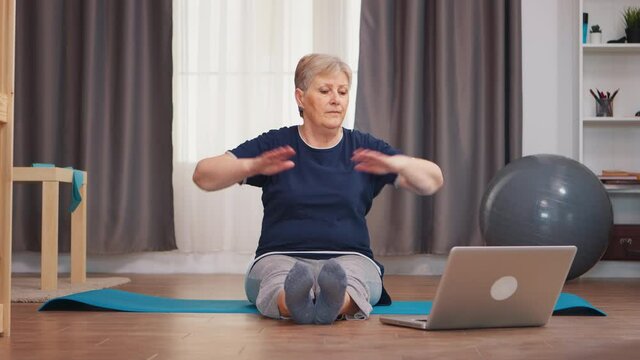Senior woman sitting on yoga mat stretching boyd sitting on mat. Online learning and study, Active healthy lifestyle sporty old person training workout homem wellness and indoor exercising