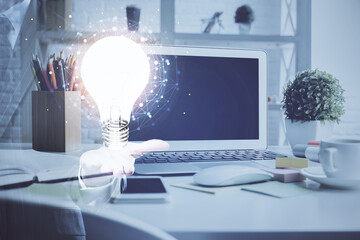 Computer on desktop in office with bulb icon hologram. Double exposure. Concept of idea.