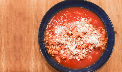 Top view of bowl of pasta fusilli with tomato sauce, parmesan cheese on top. Wooden table background with copy space for text