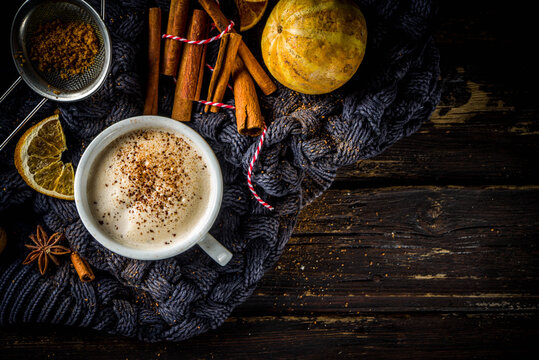 Autumn sweet hot drink, Chai Buttered Rum, Pumpkin Pie or Pumpkin Spice Coffee Latte. Cozy autumn background with traditional latte cup, spices and old sweater, on rustic wooden background