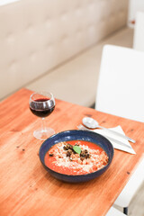 A served table with pasta in tomato sauce, parmesan and basil, a glass of red wine, on a wooden table in a restaurant 