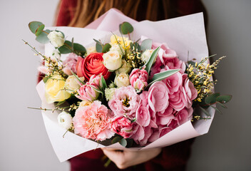 Very nice young woman holding big and beautiful bouquet of fresh hydrangea, ranunculus, carnations, eustoma, genista, eucalyptus in pink red and yellow colors, cropped photo, bouquet close up
