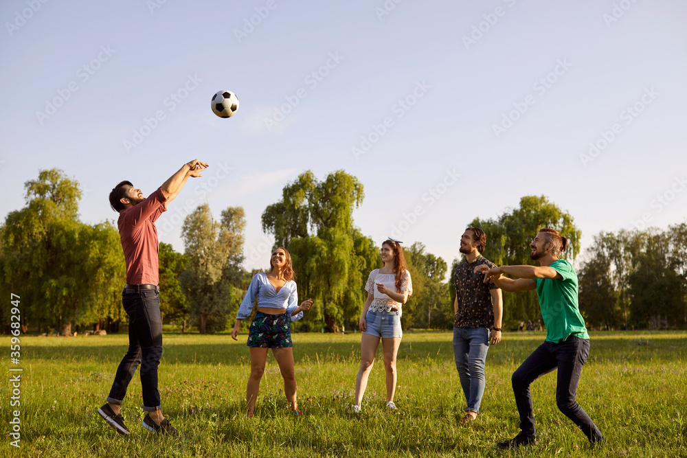 Wall mural happy friends playing volleyball game in countryside on summer day. group of students having fun tog