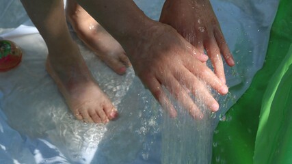 Fototapeta na wymiar hands and feet under running water and splashing water in a home pool in the muted sunlight of a summer day