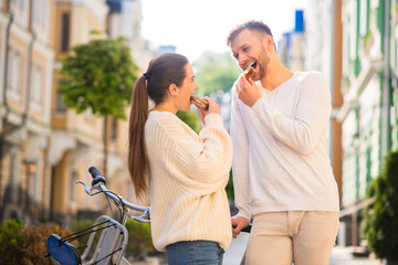 Fototapeta premium Cheerful man and woman biting sandwiches on the street