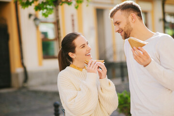 Young man and woman chatting on the street with sandwiches
