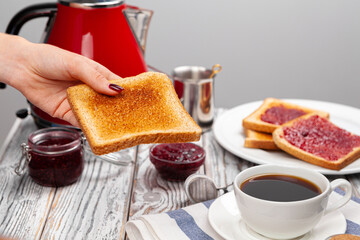 Female hand spresding strawberry jam on baked toast