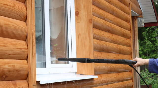 washing the facade and windows of the house with the help of a kercher in the hand of a man in blue clothes