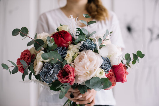 Very nice young woman holding big and beautiful bouquet of fresh roses, carnations, peony, eucalyptus in white blue and red colors, cropped photo, bouquet close up
