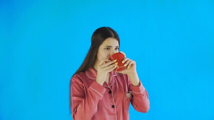 Young woman in pajamas is drinking tea or coffee on blue background in studio