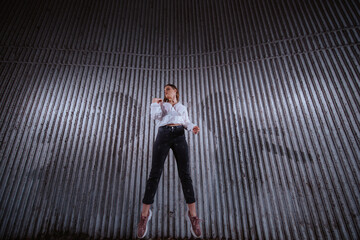 A beautiful young caucasian  girl in a white shirt in front of a ribbed wall jumps into the air