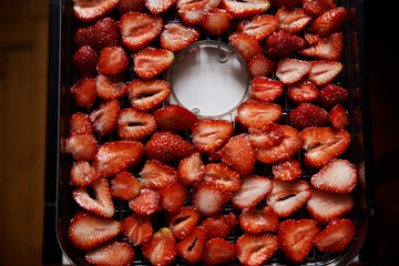 Chopped pieces of strawberries, prepared for drying, lying on white table in kitchen. Fruit dryer machine in process of making delicious snacks. Home dried berries' production. Summertime crop.