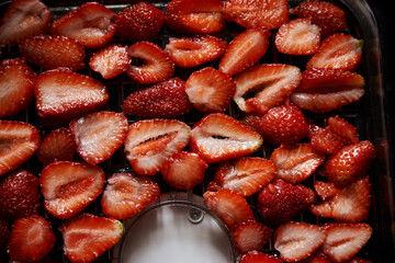 Chopped pieces of strawberries, prepared for drying, lying on white table in kitchen. Fruit dryer machine in process of making delicious snacks. Home dried berries' production. Summertime crop.