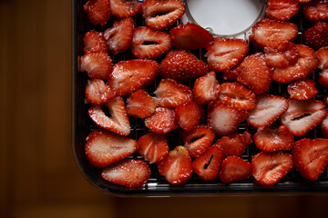Chopped pieces of strawberries, prepared for drying, lying on white table in kitchen. Fruit dryer machine in process of making delicious snacks. Home dried berries' production. Summertime crop.