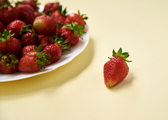White plate with strawberries on table. Close-up picture of red berries on light pale yellow background. Healthy nutrition in summertime. Juicy, rich in vitamins vegetarian food. Fruit crop.