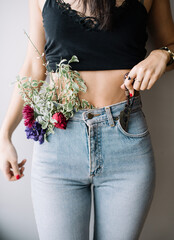 Beautiful florist young woman wearing denim pants with flowers popping from it, cropped photo