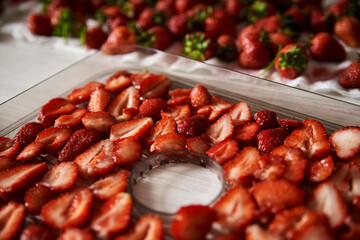 Chopped pieces of strawberries, prepared for drying, lying on white table in kitchen. Fruit dryer machine in process of making delicious snacks. Home dried berries' production. Summertime crop.