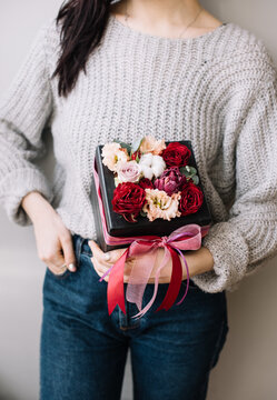 Very nice young woman holding beautiful blossoming box of ranunculus, roses, eustoma, eucalyptus, cotton flowers in white and magenta colors on the grey background