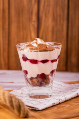 Classic tiramisu dessert with cherry in a glass on a wooden serving tray on a wooden background