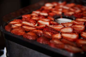 Chopped pieces of strawberries, prepared for drying, lying on white table in kitchen. Fruit dryer machine in process of making delicious snacks. Home dried berries' production. Summertime crop.
