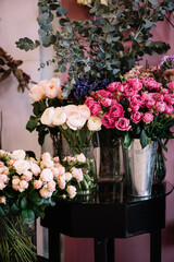Fresh delivery at the florist shop: vases with blossoming roses, eucalyptus, carnations, ranunculus flowers 