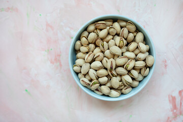 Roasted salted pistachios in shell in bowl on pink background, concept of healthy eating vegan food. Top view, selective focus, copy space