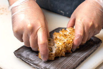 Sushi chef lays out a roll in tuna shavings on a rectangular plate