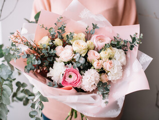 Very nice young woman holding a beautiful blossoming flower bouquet of fresh genista, roses, eucalyptus, carnations, hyacints, ranunculus in tender pink color on the grey wall background © anastasianess