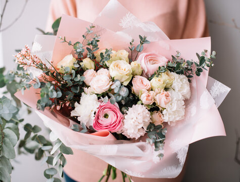 Very nice young woman holding a beautiful blossoming flower bouquet of fresh genista, roses, eucalyptus, carnations, hyacints, ranunculus in tender pink color on the grey wall background