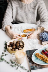 Very nice young woman sitting in a cafe, having a cup of espresso coffee coffee with some fresh eclairs, chocolate candies, eucalyptus, blue hyacinths bouquet and cappuccino cup on the white table 