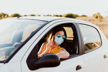 young woman in a car using mobile phone, wearing protective mask. Summer season. prevention corona virus concept