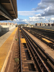 Looking down the overground subway tracks at an empty subway platform in Queens, NY. Empty subway platform.  Blue sky with clouds. Outdoor subway station stop in New York City.