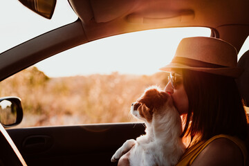 Happy young woman in a car with her dog at sunset. Travel concept