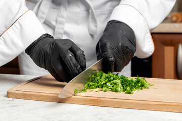 The cook cuts parsley on a wooden Board in the kitchen