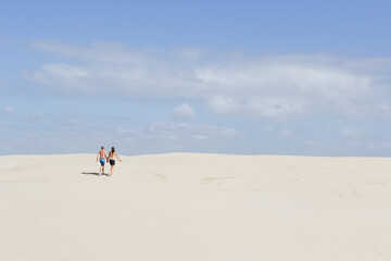 Fototapeta na wymiar Rear view of caucasian couple walking hand in hand up sand dune.