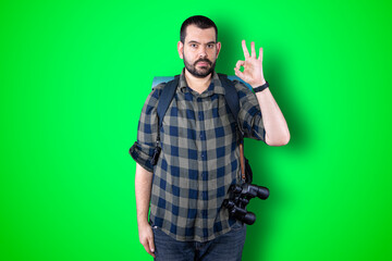Portrait of a cheerful young traveler man showing okay and victory gesture isolated on the chroma background