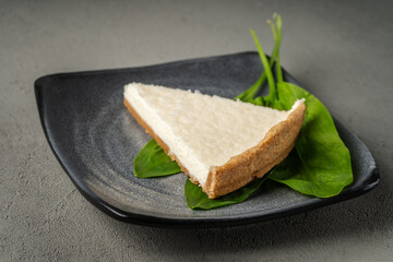 Vegetarian cheesecake on a gray plate with green leaves