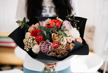 Very nice young woman holding huge beautiful blossoming bouquet of fresh roses, carnations, peony, ganista, statice  in brown and red colors on the grey background