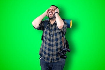 Portrait of a puzzled bearded traveler man holding hands on his head isolated over chroma background