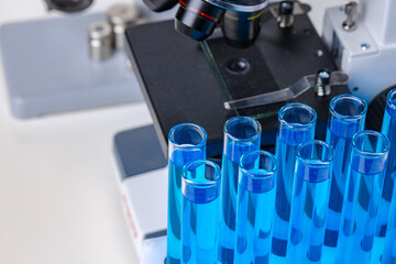 Close up of laboratory microscope with set of test tubes with blue liquid