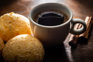 Xícara branca de louça com café e pães de queijo.