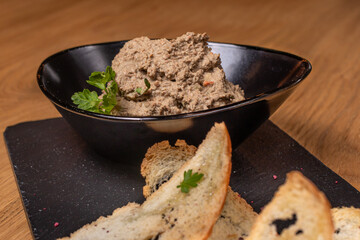 Pate of beef liver and meat with herbs in a black plate with crunchy toast. Restaurant food.