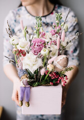 Very nice young woman holding easter themed beautiful blossoming box of fresh ranunculus, matthiola, roses in white and pink colors on the grey background
