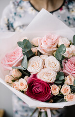 Very nice young woman holding beautiful blossoming bouquet of fresh roses, ranunculus, eucalyptus in pink colors on the grey background