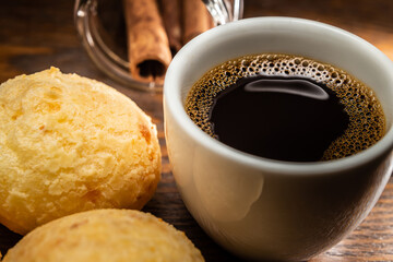 Xícara de café com pães de queijo e palitos de canela.